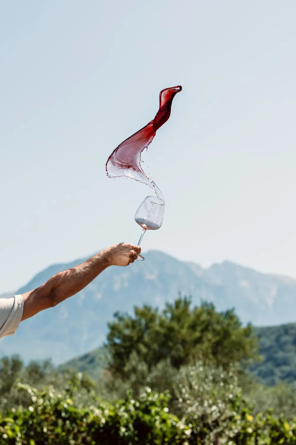 Red wine flung from a glass in an arc against the sky, Tomorri behind