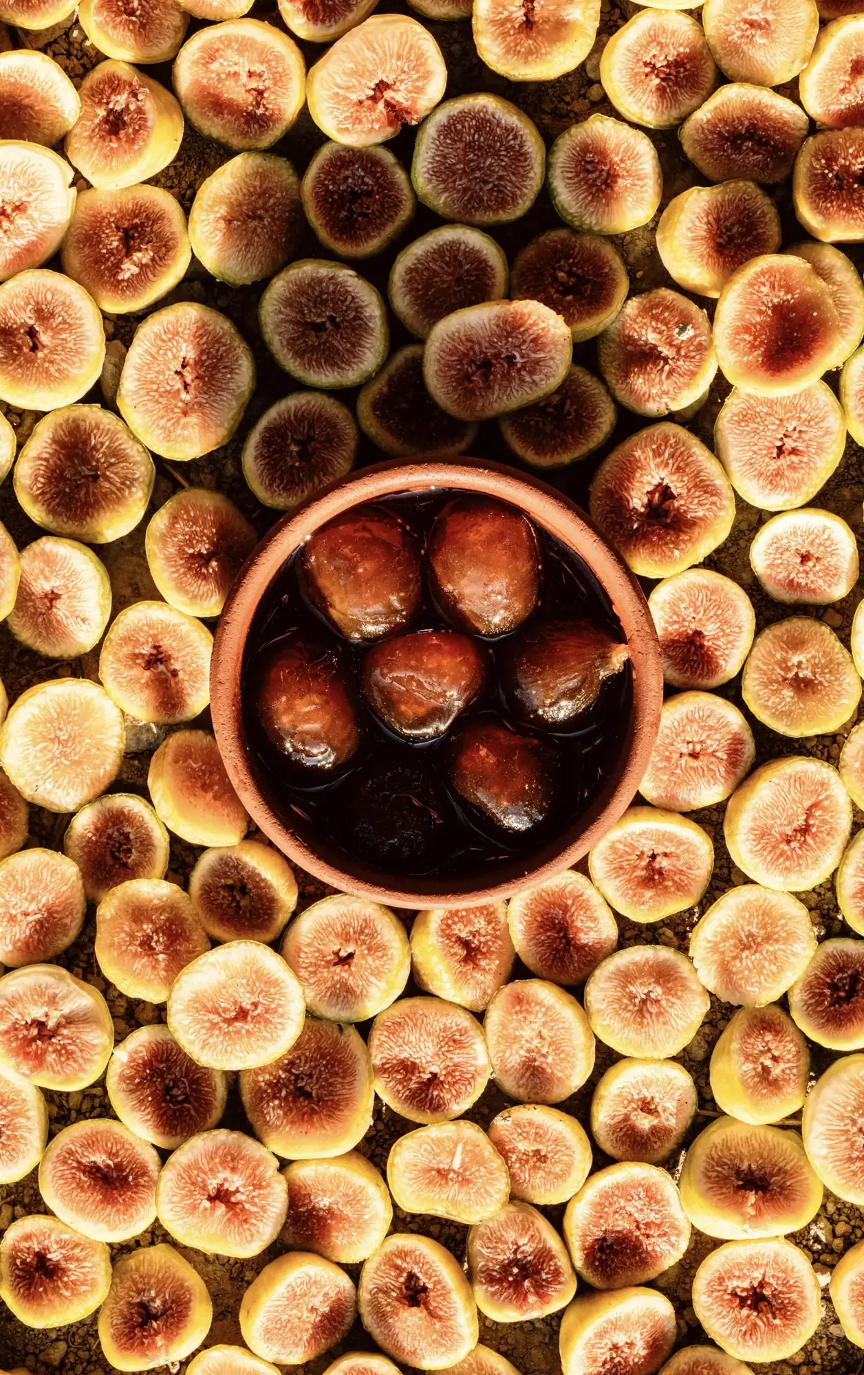 Halved figs around a clay bowl of whole figs in syrup, a fig gliko made in our kitchen