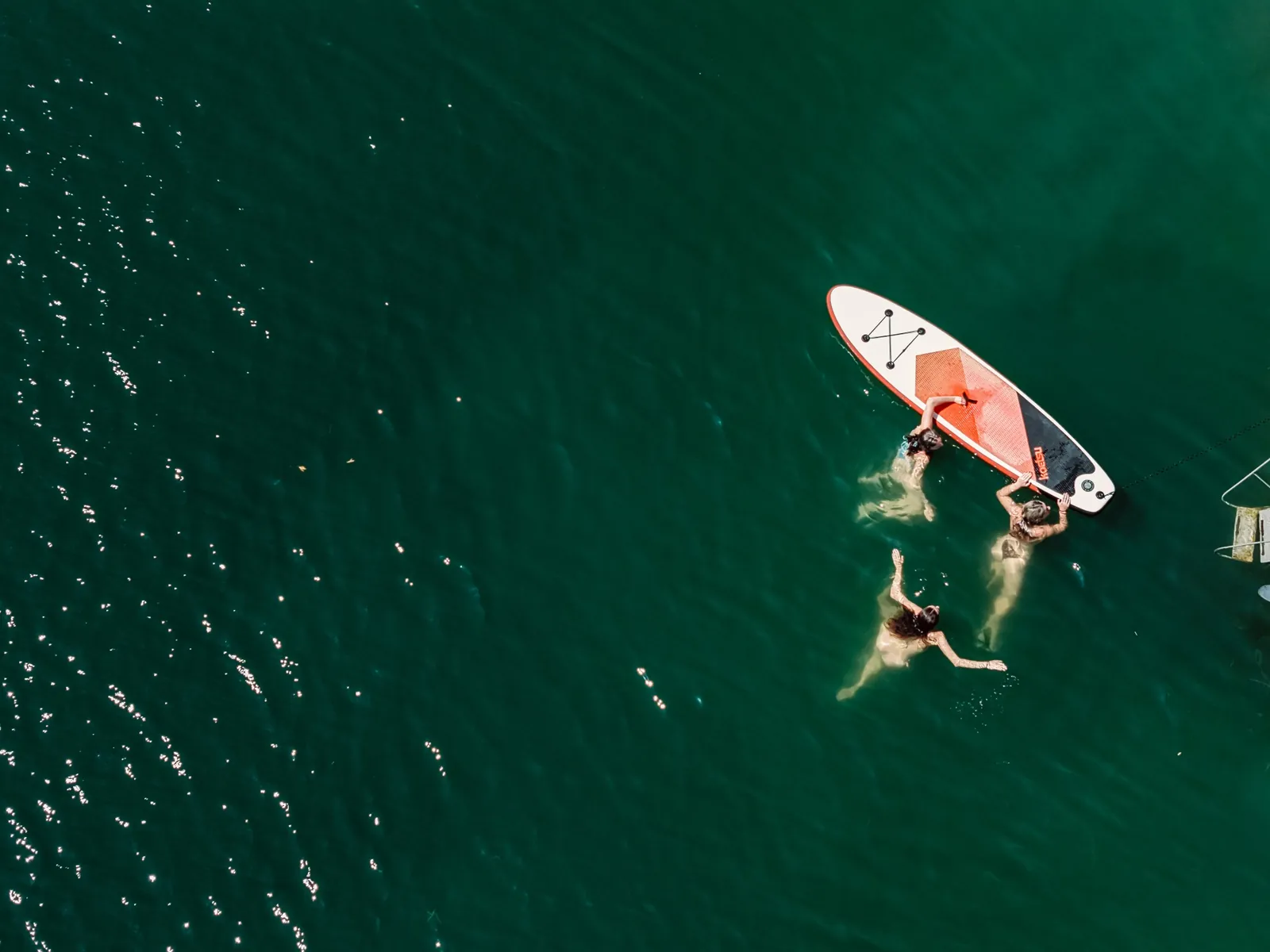 Swimmers and a paddleboard on the green water of the lake, seen from above