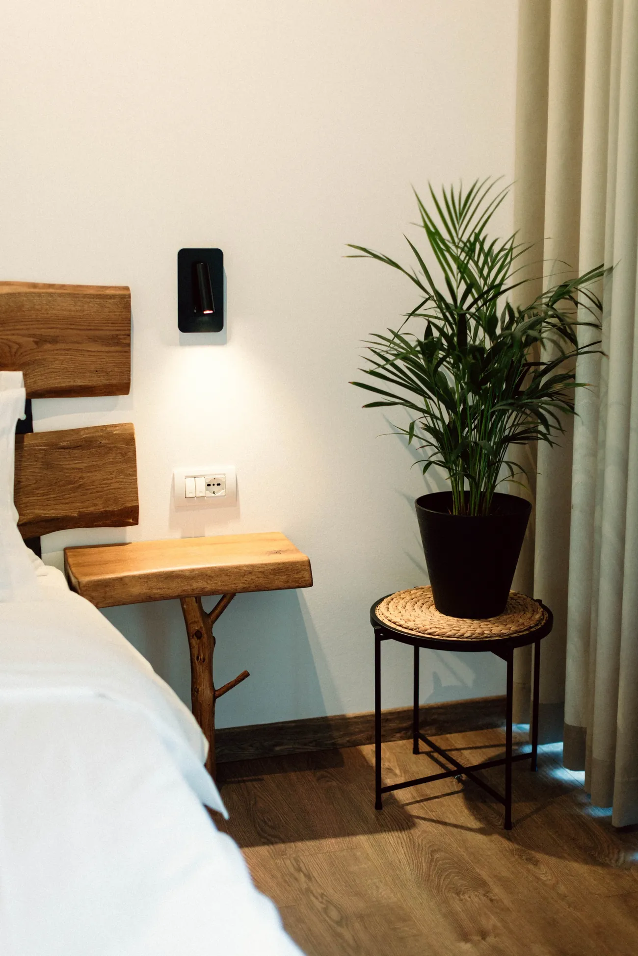 A guest room: an oak headboard, a bedside shelf on a branch, a palm by the curtain