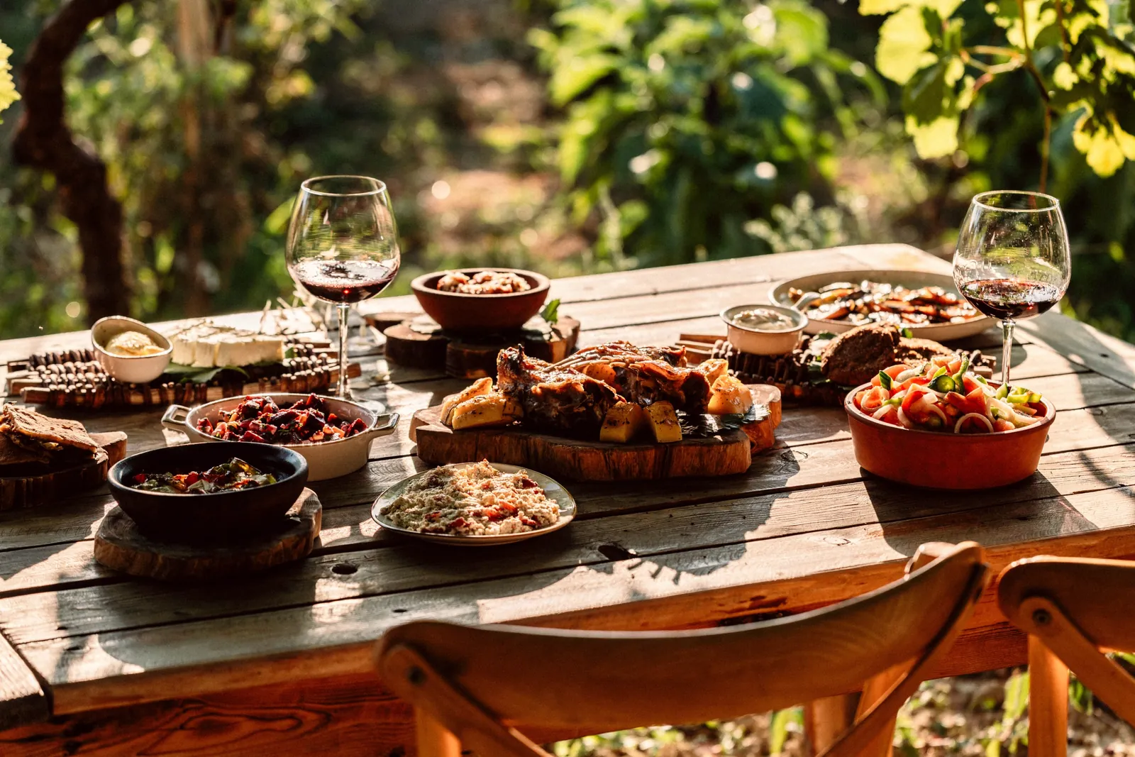 A wooden table set for lunch with wine glasses, shared starters and bread